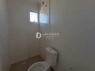 Vista de um corredor interno com uma porta e um vaso sanitário em uma residência.