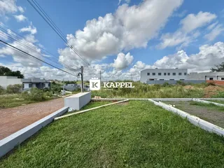 Vista externa de um terreno com gramado e estruturas ao fundo.