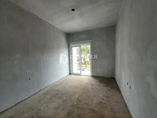 Interior de um cômodo vazio com paredes brancas e piso de terra.