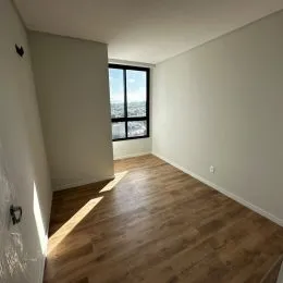 Foto interna mostrando um ambiente com piso de madeira e uma janela com vista.