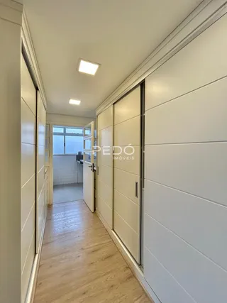 Corredor interno de uma residência com piso de madeira clara e paredes brancas.