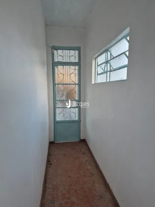 Corredor interno com paredes brancas e piso de terracota.