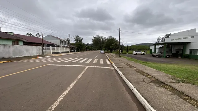 Vista externa de uma rua residencial em Lajeado, com casas e um clube esportivo ao fundo.