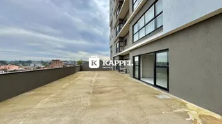 Vista externa de um prédio residencial com fachada em tom neutro e uma área de terraço pavimentada.