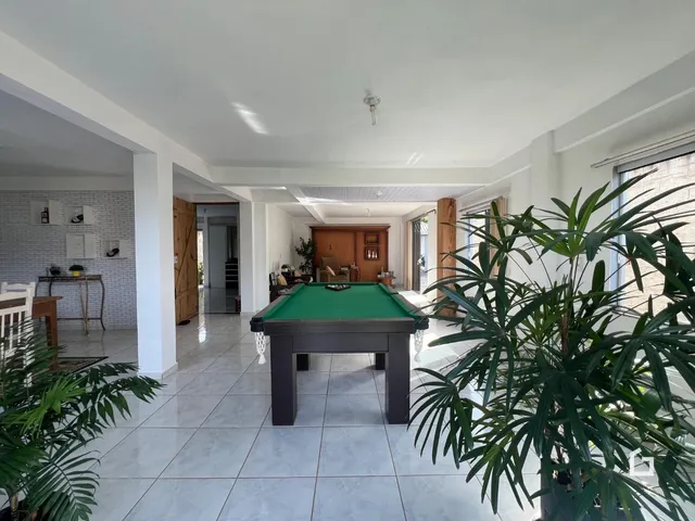 Ambiente interno de uma sala ampla com mesa de bilhar e piso de cerâmica.