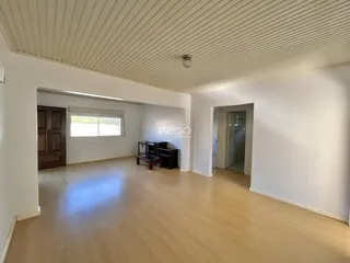 Espaço interno amplo com piso de madeira clara e paredes brancas.