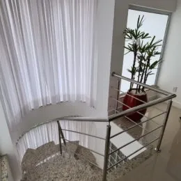 Vista de um corredor com guarda-corpo metálico e cortinas brancas.