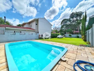 Foto de uma piscina azul em um quintal com gramado e residência ao fundo.