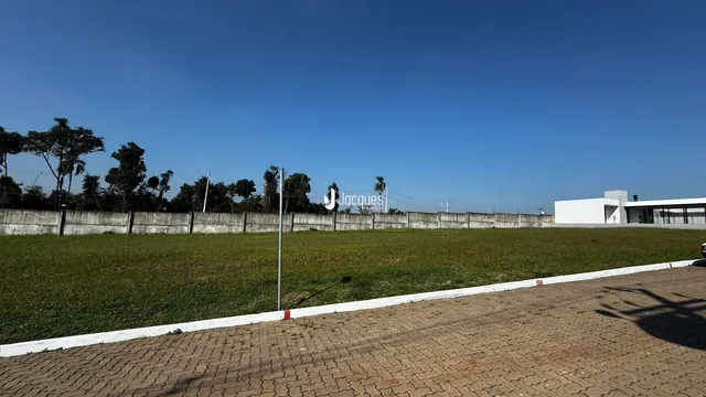 Vista externa de um terreno gramado com muro e cerca.