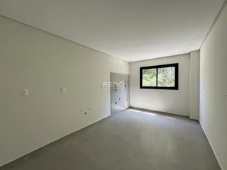 Ambiente interno de uma sala ampla com paredes brancas e piso de concreto.