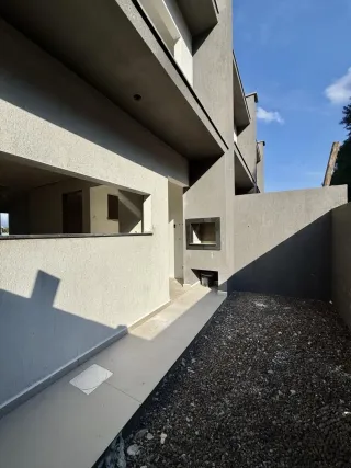 Fachada externa de um prédio residencial com área de concreto e pátio de cascalho.