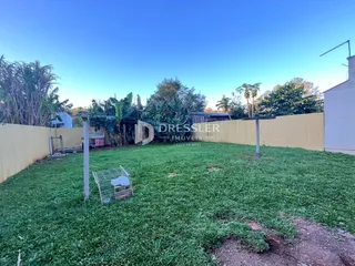Vista externa de um terreno gramado com cerca e vegetação.
