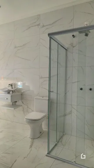 Banheiro com box de vidro e revestimento branco.
