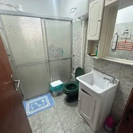 Banheiro com box de vidro e piso cerâmico claro.