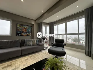 Sala de estar com sofá e vista panorâmica da cidade através das grandes janelas.