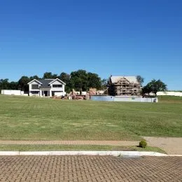 Vista externa de uma propriedade com um campo gramado e árvores ao fundo.