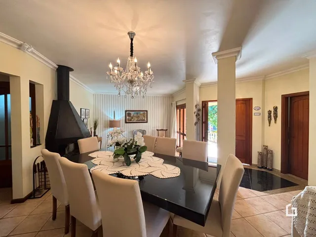 Uma sala de jantar com mesa escura e cadeiras brancas é visível.