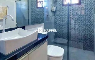 Banheiro com bancada escura, pia branca e box de vidro transparente.