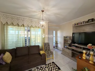Sala de estar com sofá marrom e janela com cortinas claras.