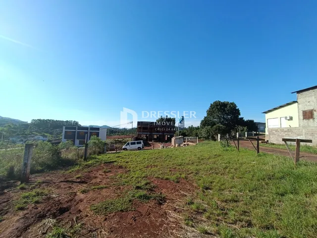 Paisagem de um terreno com vegetação e estruturas ao fundo.