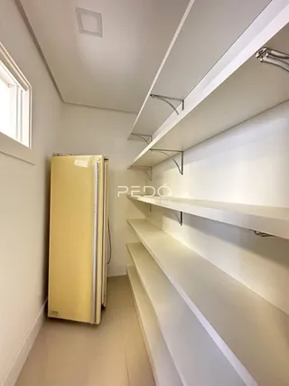 Interior de um corredor com geladeira e prateleiras em uma residência.