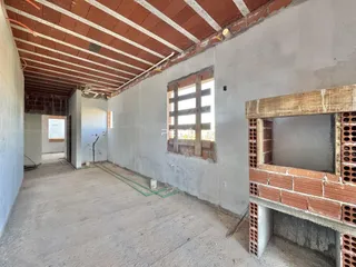 Vista de um corredor interno em construção com paredes de alvenaria e teto de madeira exposto.
