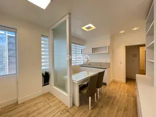 Ambiente interno de uma sala de estar com piso de madeira clara e área de banho em vidro.
