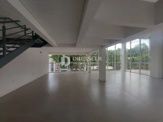 Ambiente interno de uma sala ampla com grandes portas de vidro que dão acesso a uma área externa.