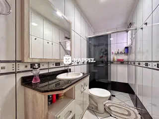 Banheiro com bancada de granito e box de vidro transparente.