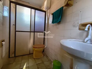 Foto interna de um banheiro com azulejos brancos e uma porta de vidro.