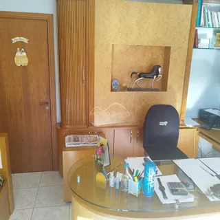 Foto de um escritório interno com mesa de vidro e estante de livros.