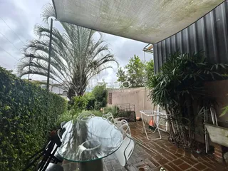 Uma área externa coberta com mesa de vidro e vegetação exuberante.