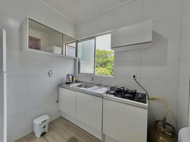 Cozinha com armários brancos e piso de madeira clara.