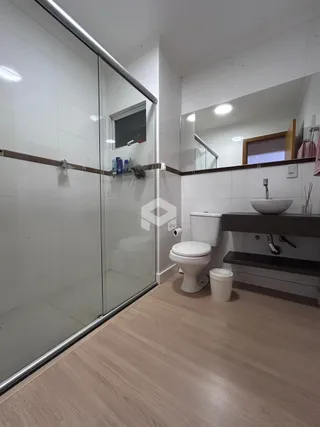 Foto de um banheiro com piso de madeira clara e divisória de vidro.