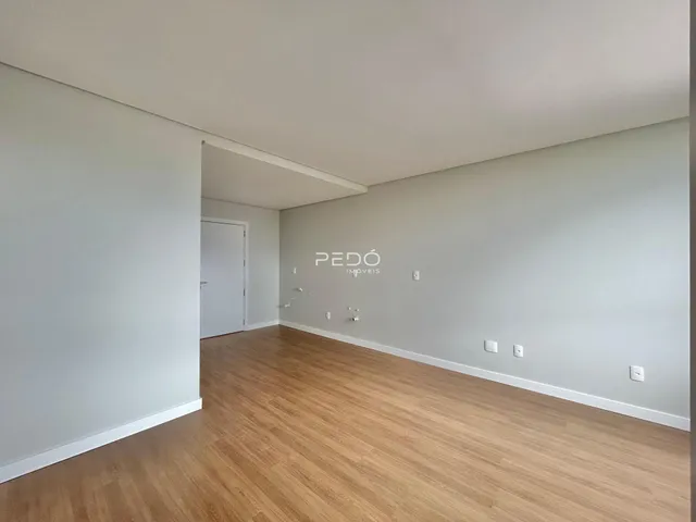 Ambiente interno de uma sala com piso de madeira clara e paredes brancas.