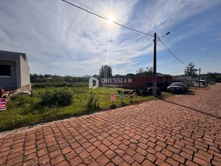 Vista externa de um terreno com pavimentação de tijolos e vegetação.