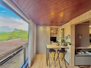 Sala de estar com piso de madeira e vista para a vegetação externa.