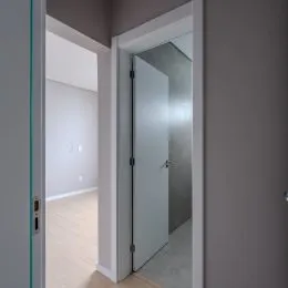 Vista de um corredor interno com porta branca e acabamento neutro.