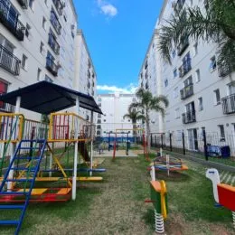 Área externa com gramado e equipamentos de playground em um condomínio.