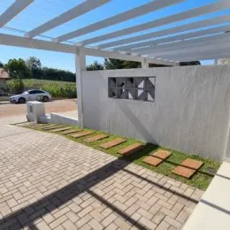 Vista externa de um pátio pavimentado com estrutura de pergolado branco.