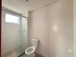 Ambiente de banheiro com revestimento cerâmico branco e box de vidro.