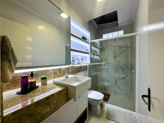 Interior de um banheiro com bancada de mármore e box de vidro.