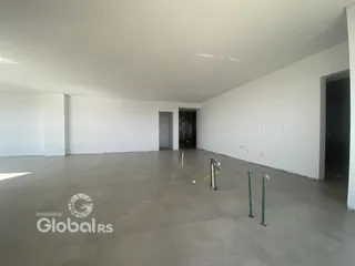 Interior de uma sala ampla e vazia com paredes brancas e piso claro.