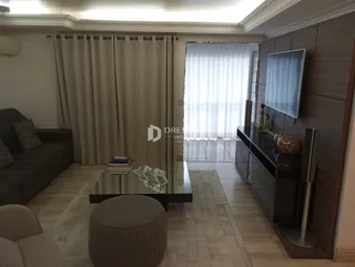Sala de estar com piso de madeira e grandes janelas cobertas por cortinas brancas.