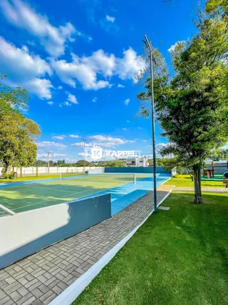 Foto de uma quadra esportiva externa com gramado e árvores em um dia ensolarado.