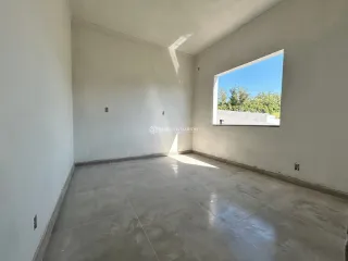 Ambiente interno com paredes brancas e piso de concreto, com vista para o exterior.