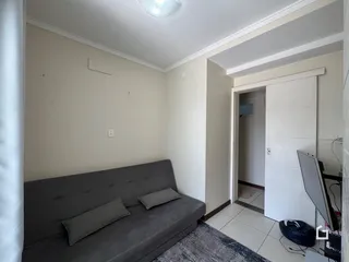 Sala de estar com sofá cinza e paredes brancas em um imóvel.