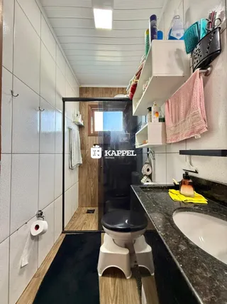 Banheiro com revestimento branco e box de vidro transparente.
