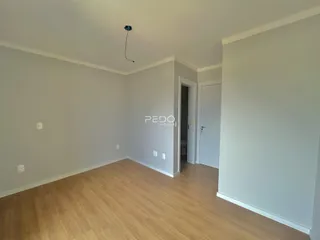 Vista interna de uma sala com piso de madeira clara e paredes brancas.