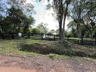 Vista externa da propriedade com cerca de madeira e vegetação densa.